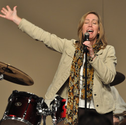 Female singing into a microphone, eyes, closed, one hand up in the air