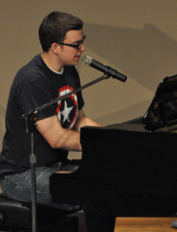 Man playing a grand piano singing into a microphone