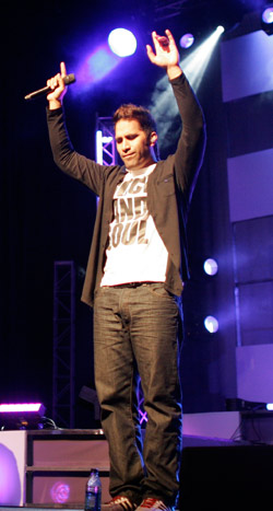 Man holding a microphone on stage with hands held up to the sky