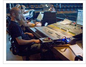 Church sund technicians sitting at the back of large worship space in front of large audio mixing boards